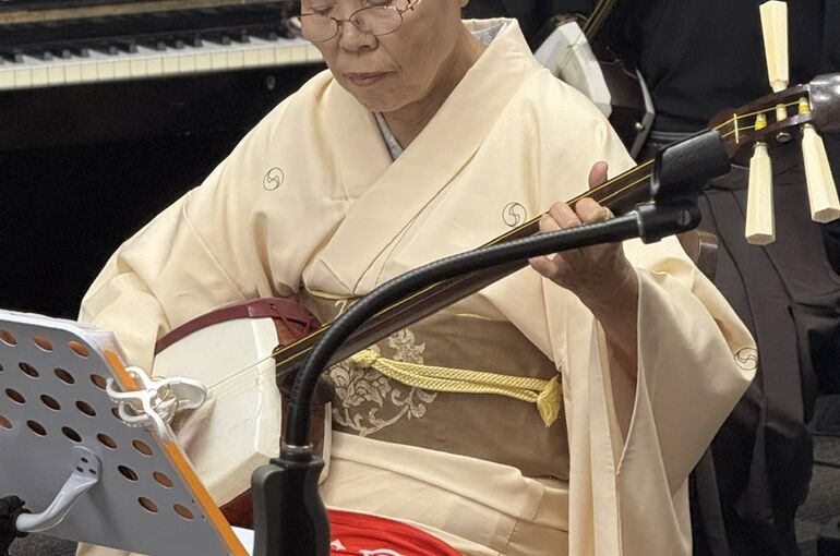着物姿で三味線を演奏するご利用者。後ろでは紋付袴の奏者が寄り添っている